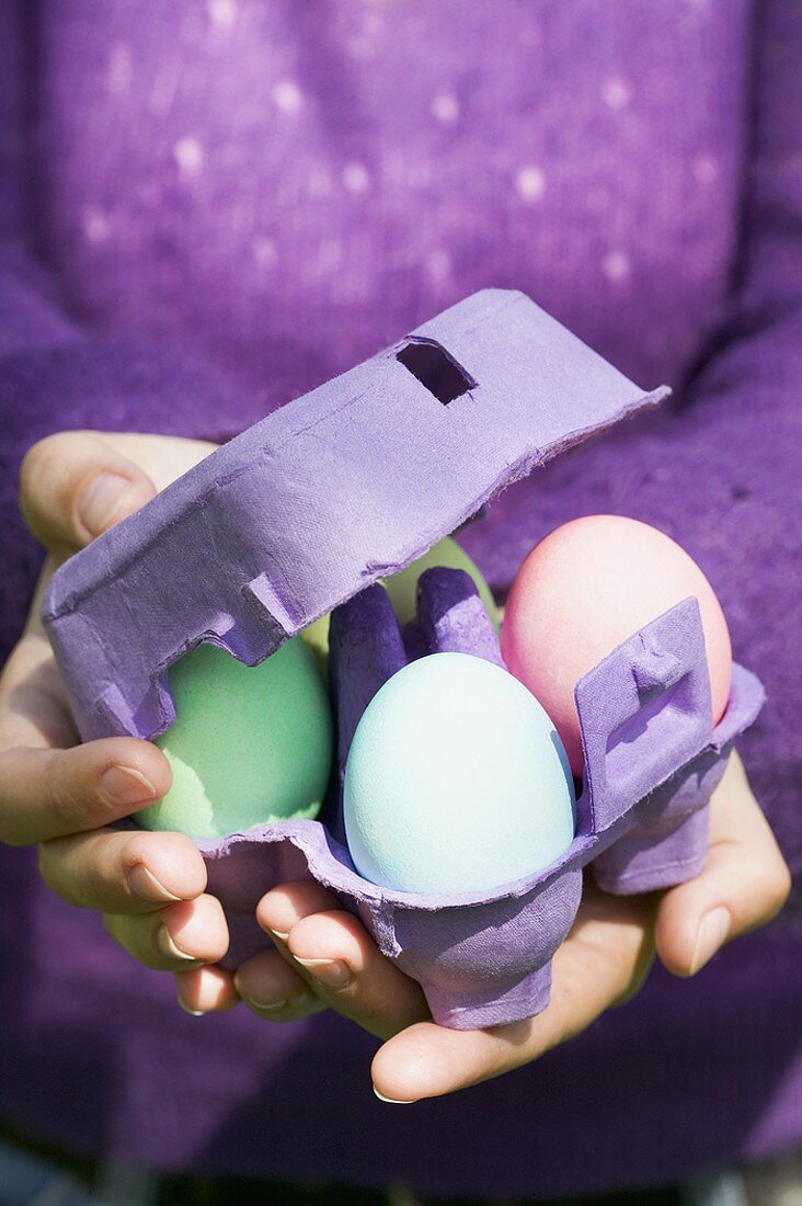 Frau hält Eierkarton mit gefärbten Eiern