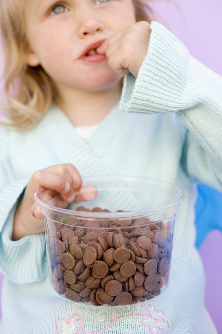 Kleines Mädchen nascht Schokotropfen aus Plastikschale