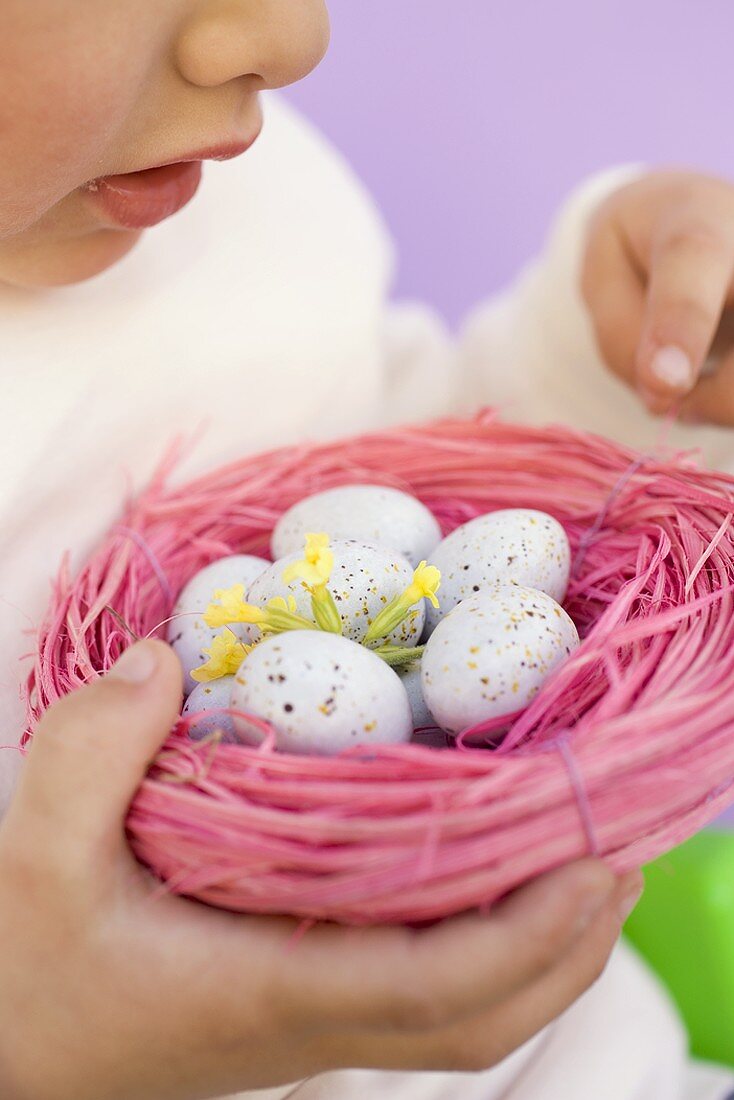 Kind hält Ostereier im rosa Nest