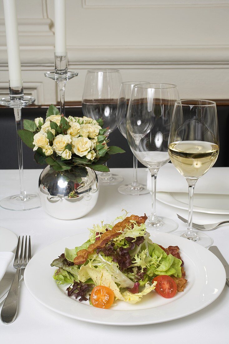 Salad with bacon & glasses of white wine on laid table