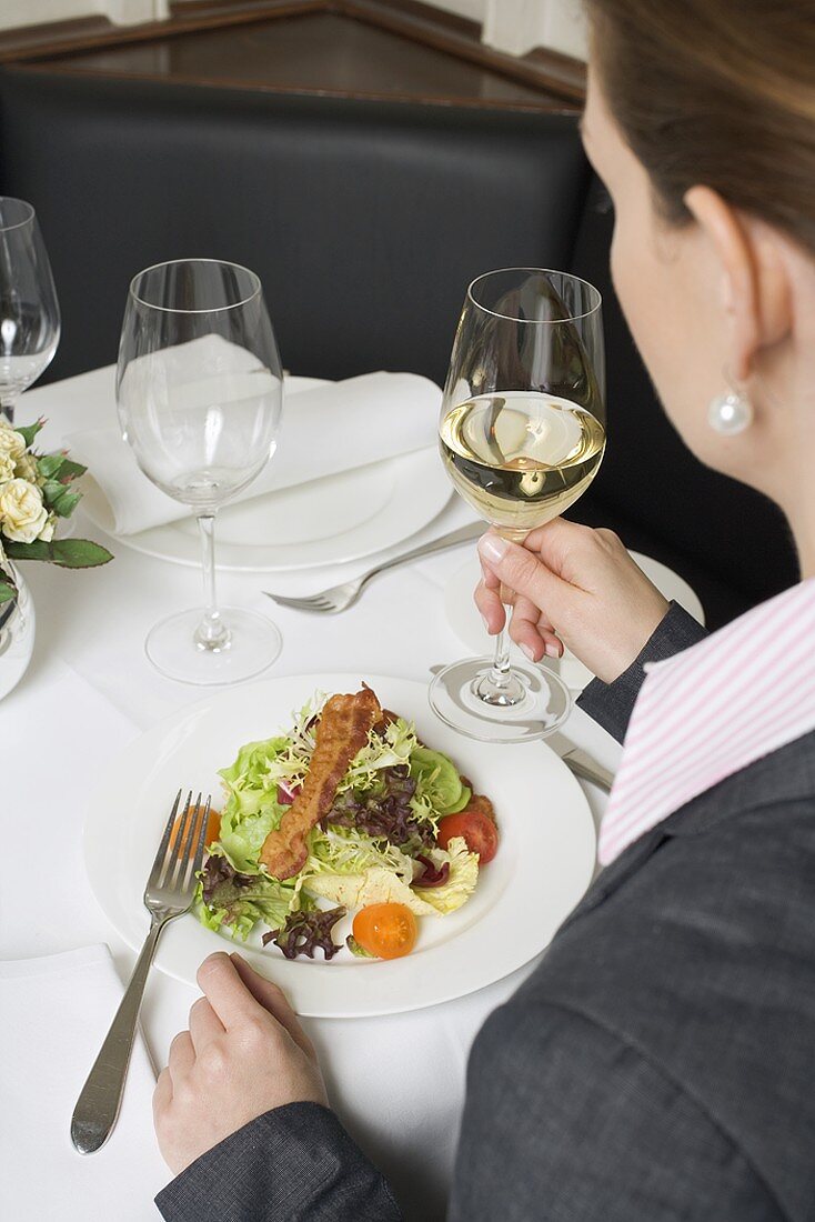 Frau trinkt Weißwein zum Salat im Restaurant