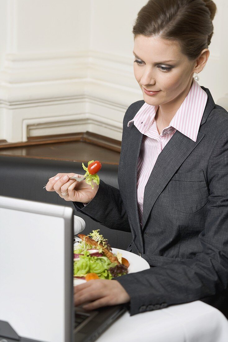 Frau isst Salat vor einem Laptop im Restaurant