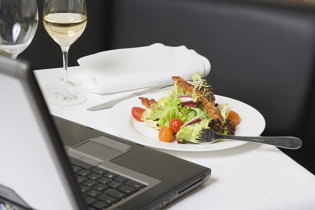 Salad with bacon in front of laptop on restaurant table