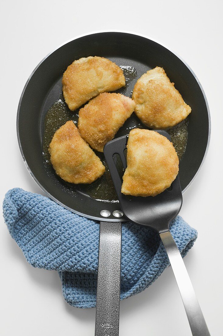 Breaded pasties in frying pan with spatula (overhead view)