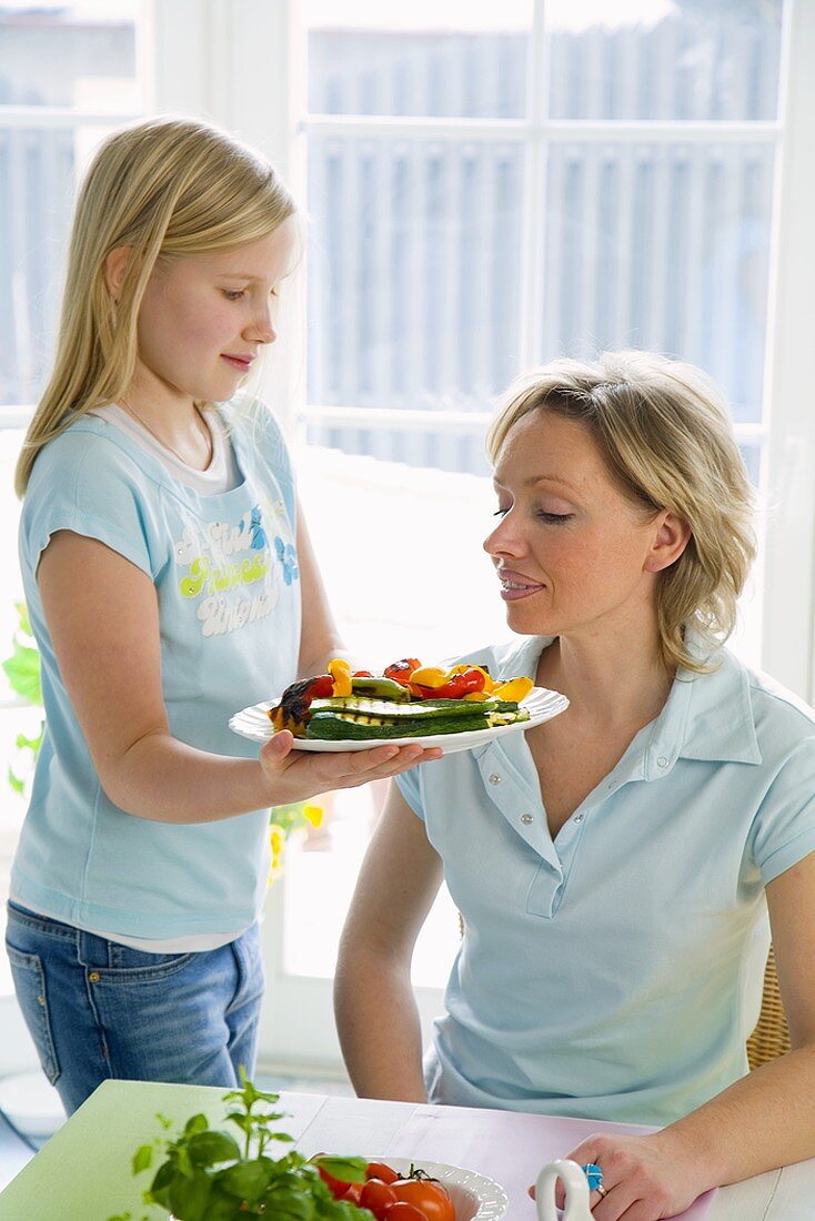 Girl serving plate of vegetables to woman