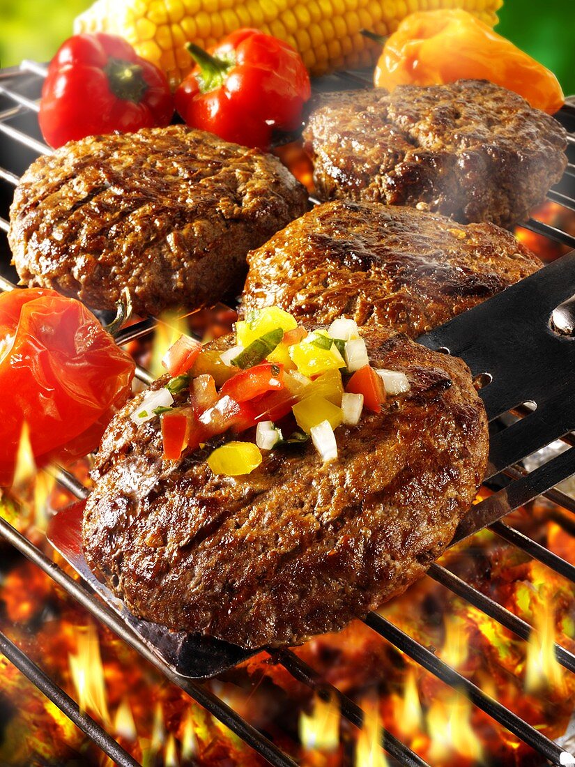 Burgers with vegetables on barbecue rack and spatula