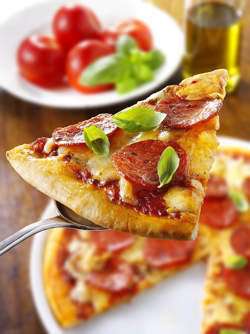 Slice of pepperoni pizza with basil on server
