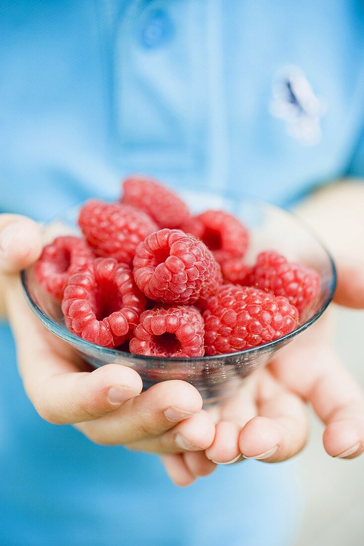 Child's hands holding glass dish of raspberries