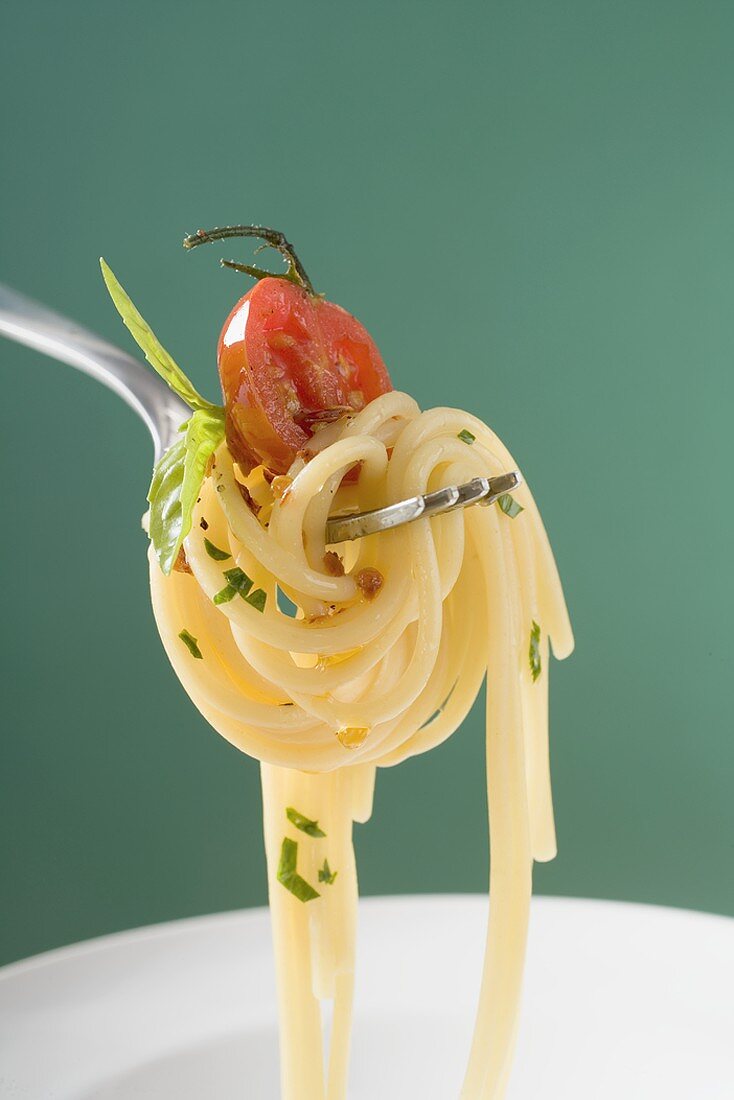 Spaghetti mit Kirschtomate auf Gabel über weißem Teller
