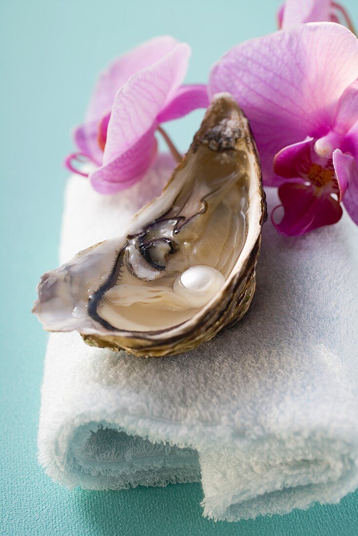Fresh oyster with pearl on towel, orchids