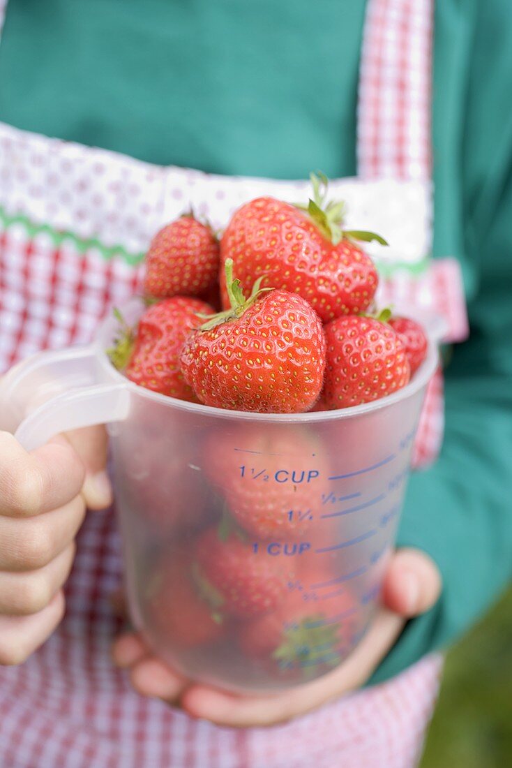 Child holding measuring jug full of strawberries