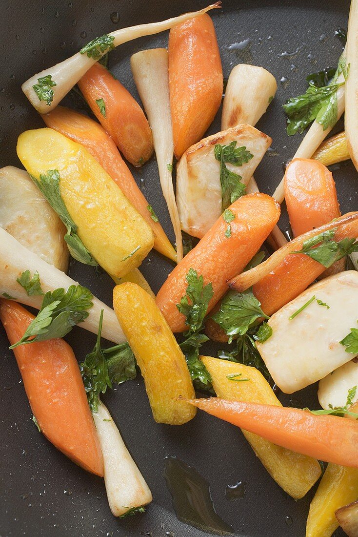 Fried root vegetables with parsley in frying pan