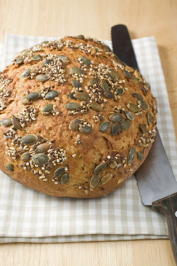 Vollkornbrot mit Kürbiskernen auf Geschirrtuch mit Brotmesser