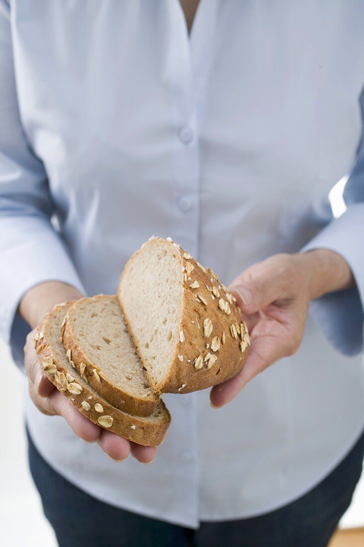 Woman holding partly sliced loaf of oat bread
