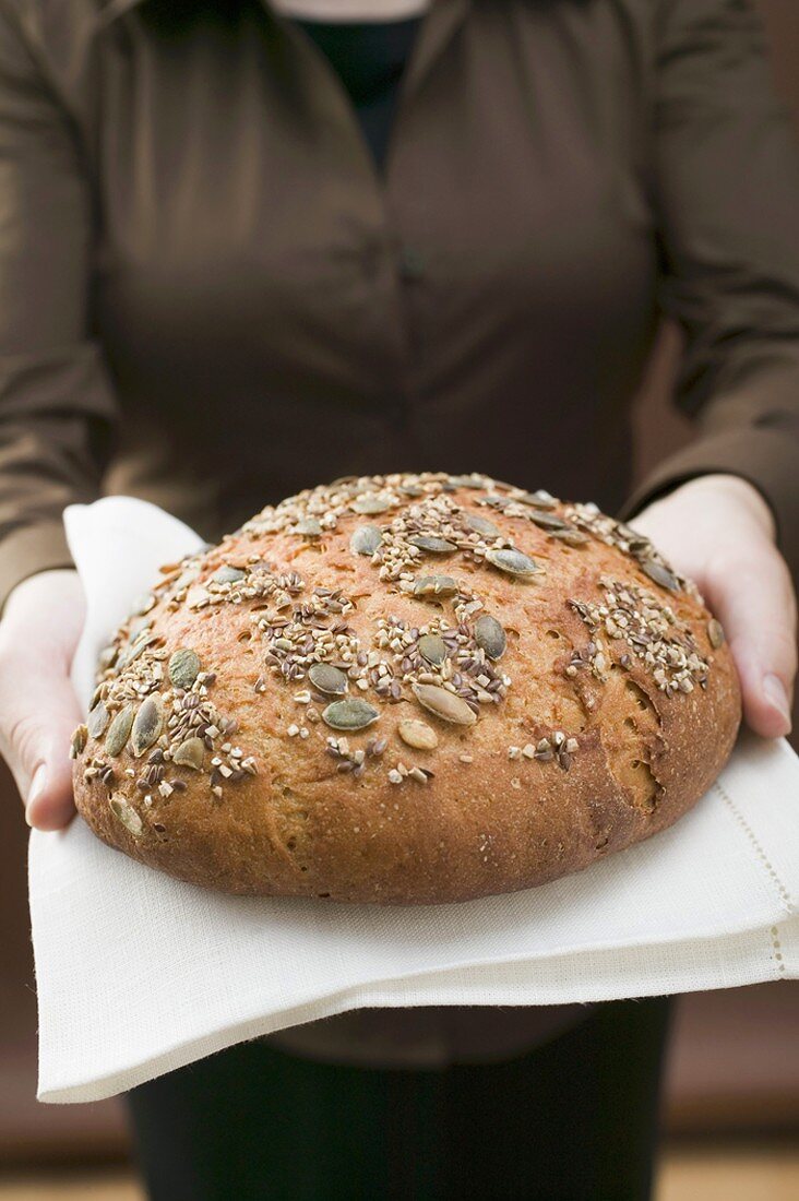 Woman holding wholemeal bread with pumpkin seeds on linen cloth