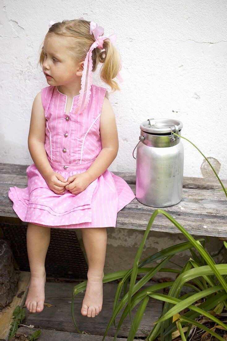 Small girl on wooden bench beside milk can
