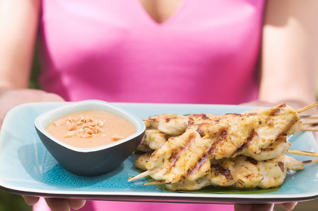 Woman holding platter of satay and peanut dip