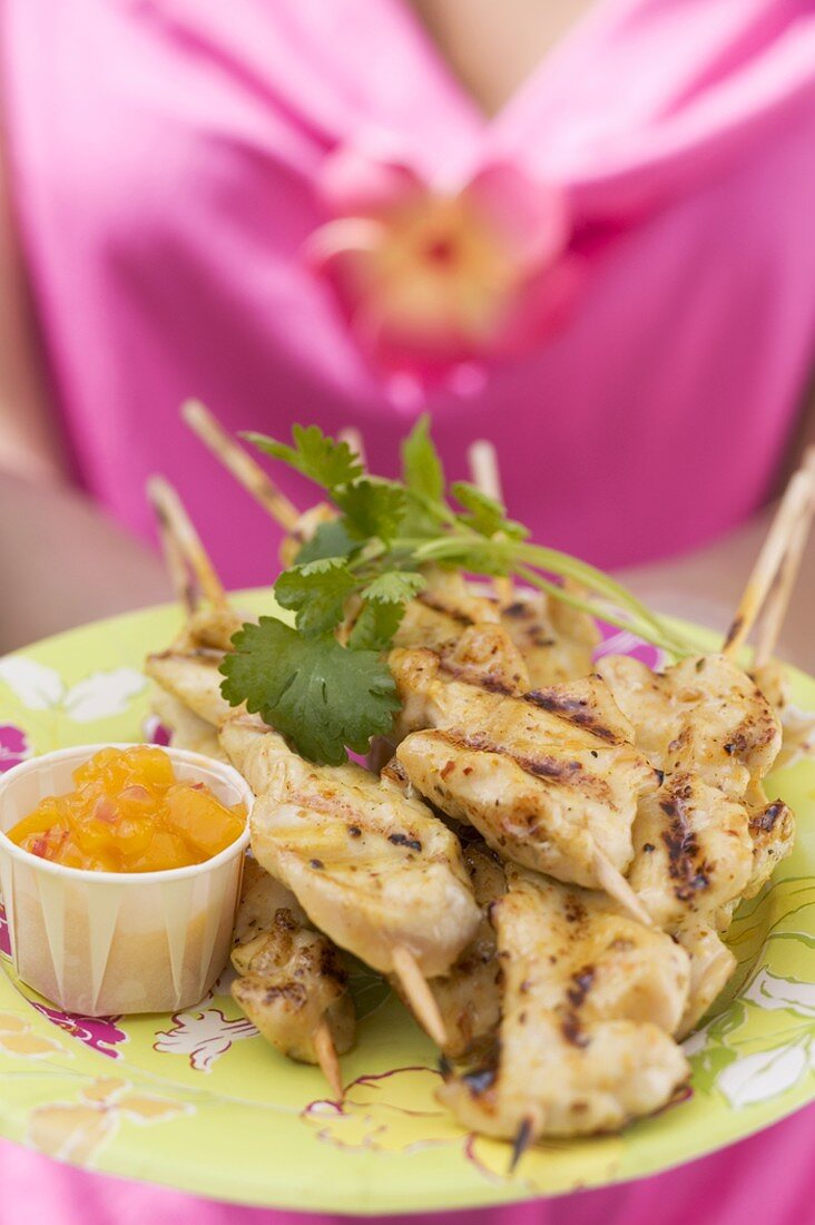 Woman holding plate of satay and chutney