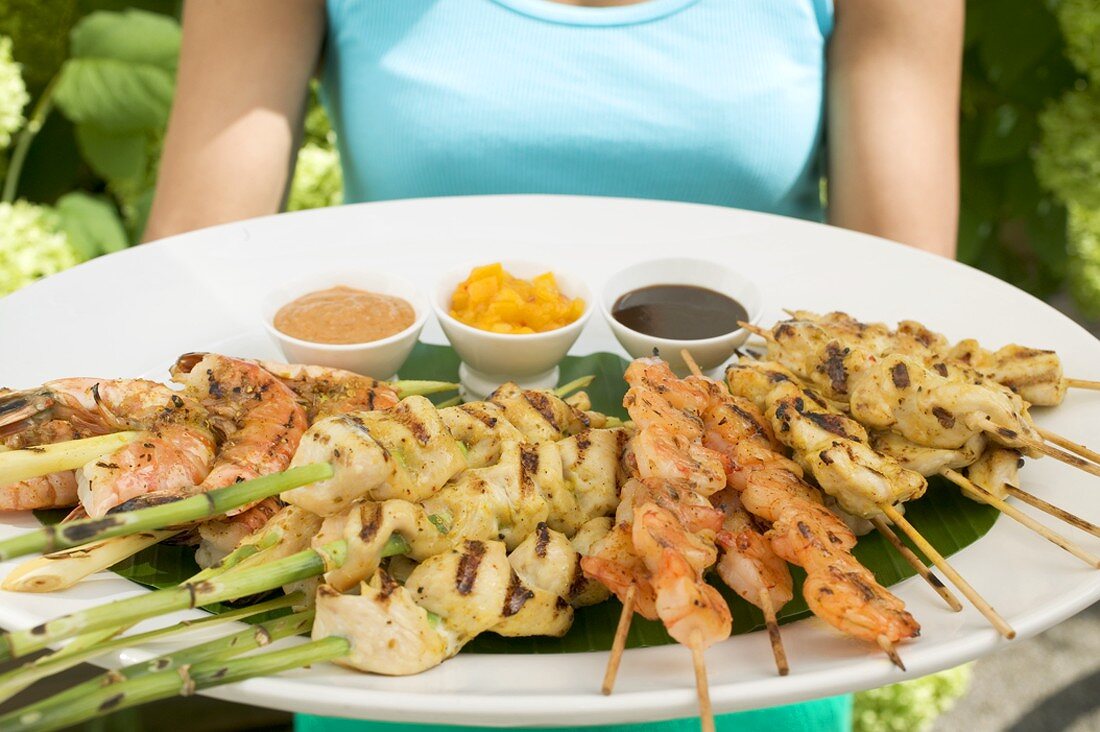 Frau hält grosse Platte mit Satespiessen und Dips