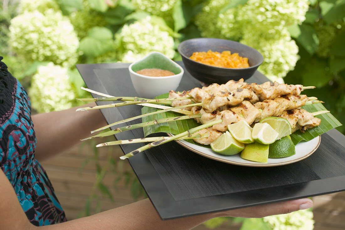 Woman holding tray of satay and dips