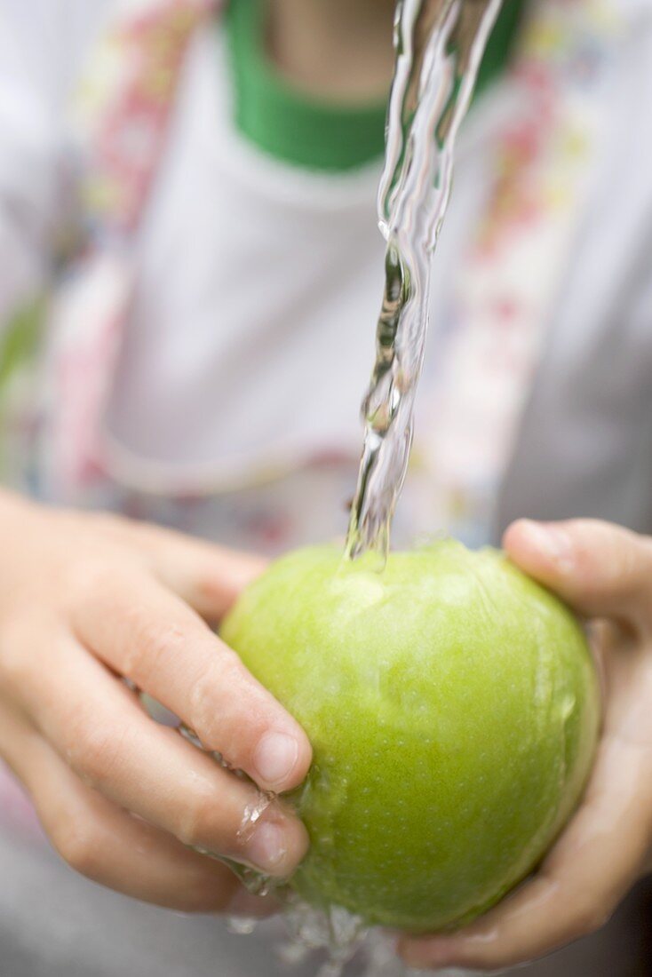 Kind hält grünen Apfel unter Wasserstrahl