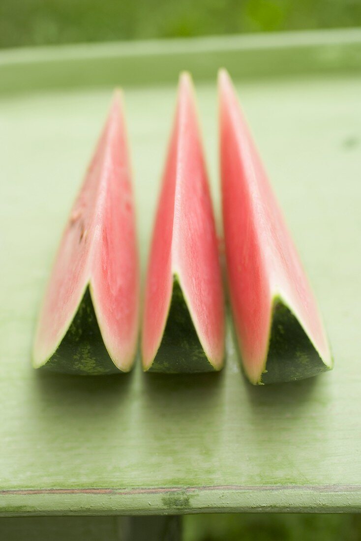 Three wedges of watermelon on green table