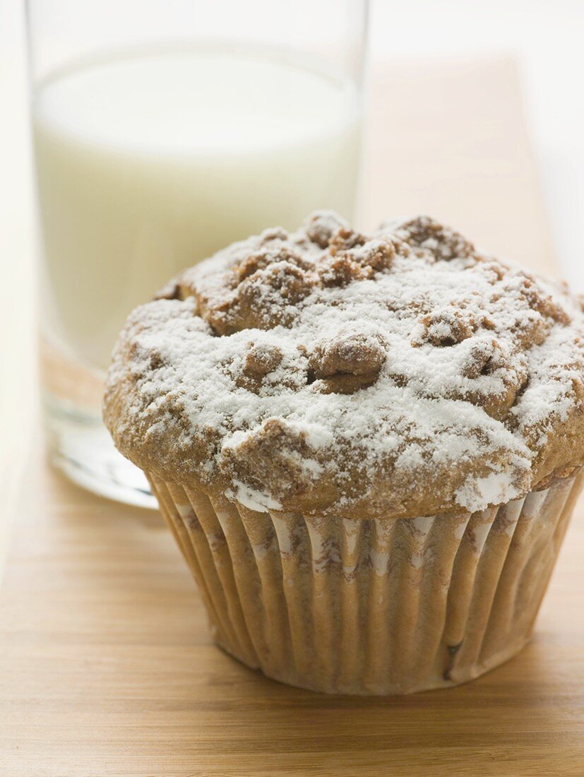 Nut muffin sprinkled with icing sugar in front of glass of milk