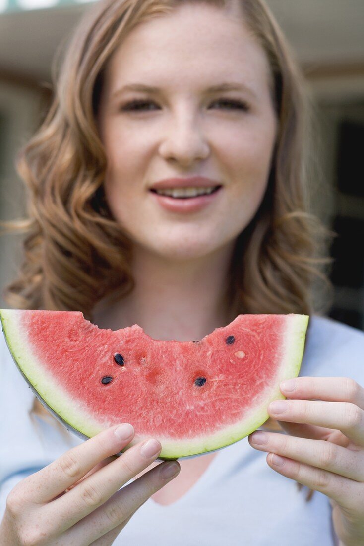 Junge Frau hält angebissene Wassermelonenspalte