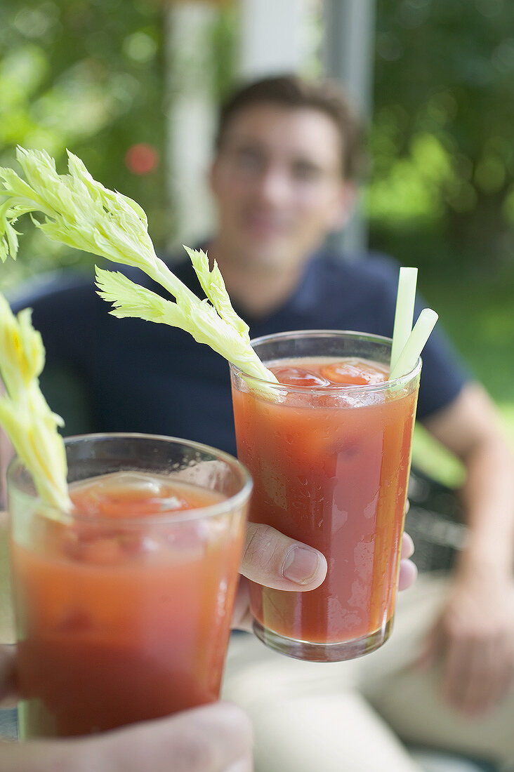 Hände halten zwei Tomatendrinks, junger Mann im Hintergrund