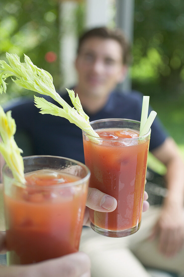 Hands holding two tomato drinks, young man in background