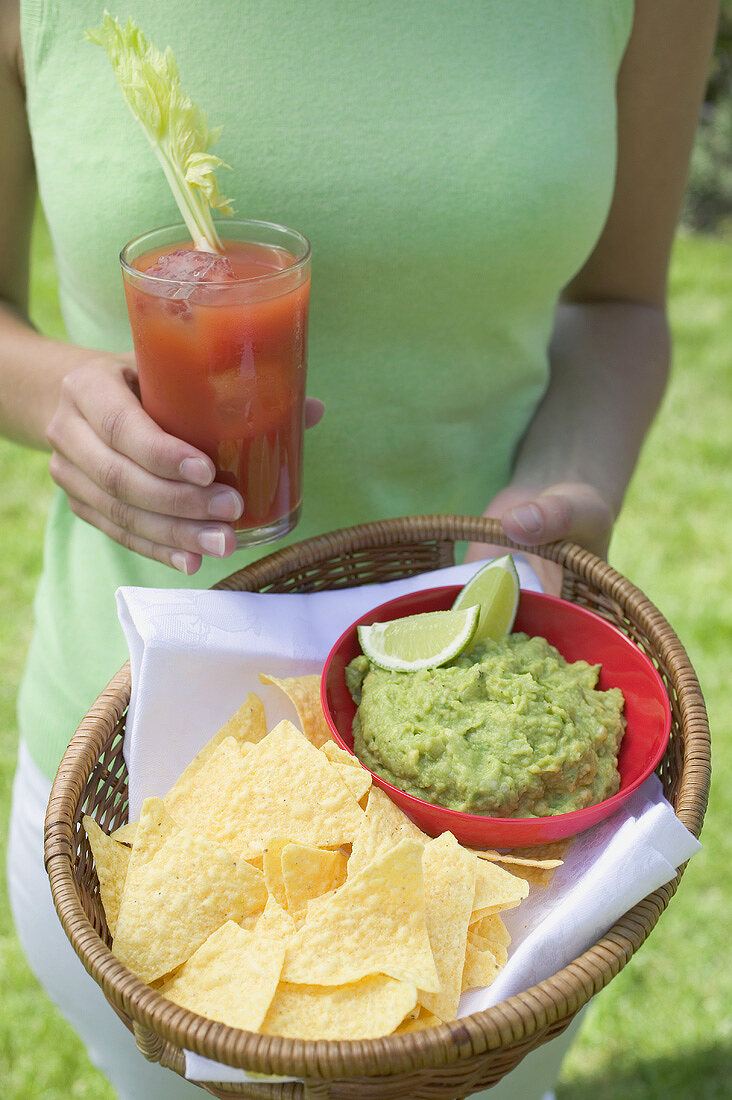 Woman holding tomato drink & basket of guacamole & chips