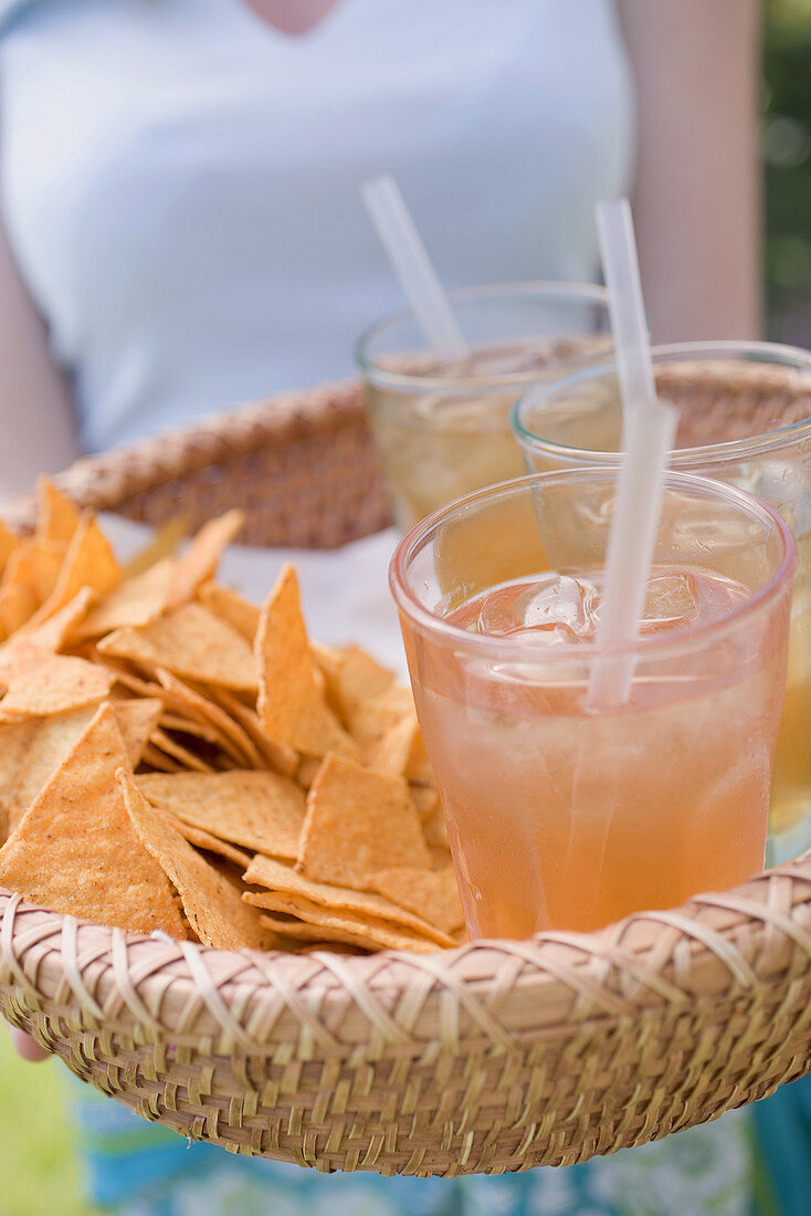 Frau serviert Korb mit Eistee und Tortillachips