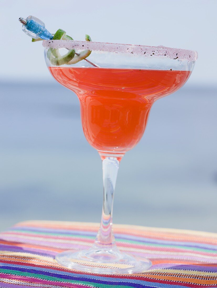 Red cocktail in glass with sugared rim, sea in background