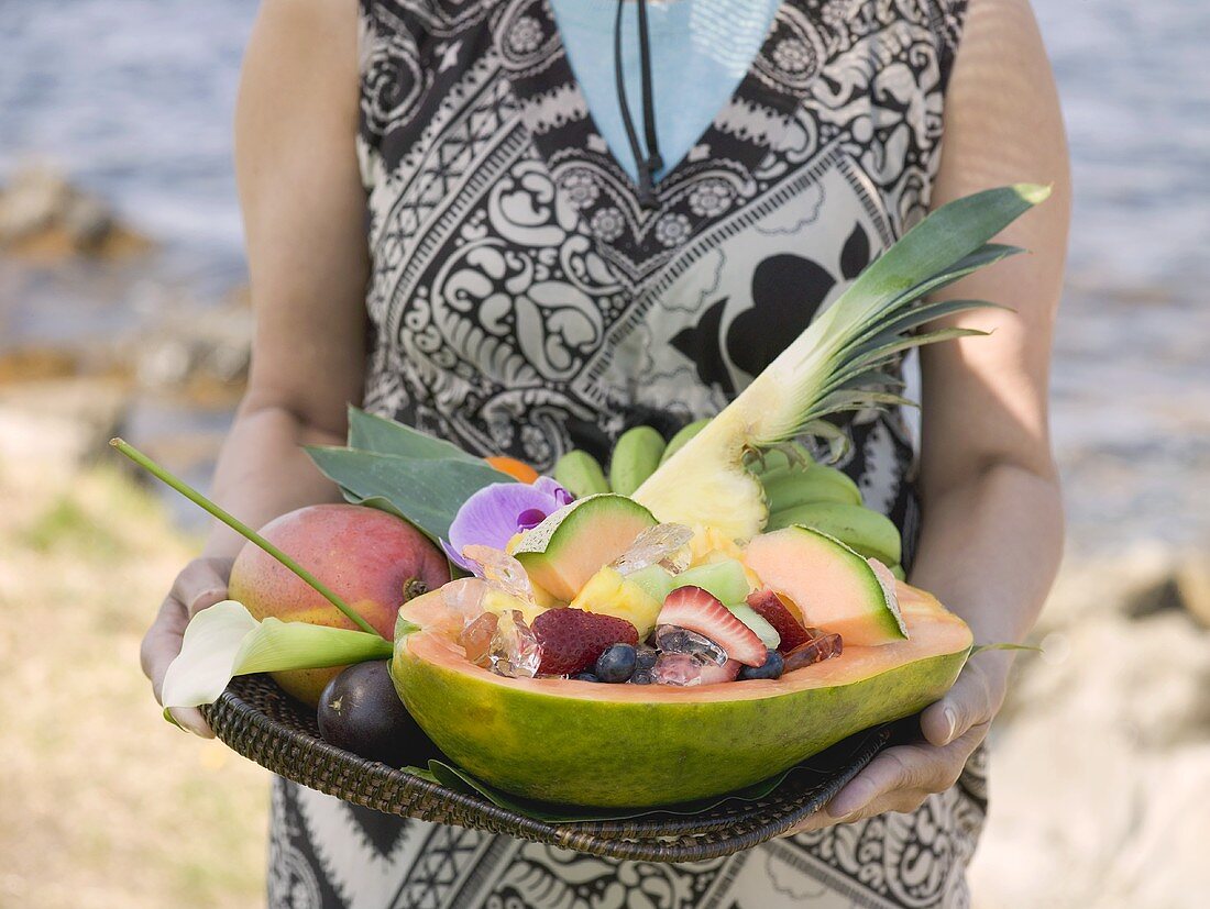 Woman holding tray of fresh exotic fruit by sea