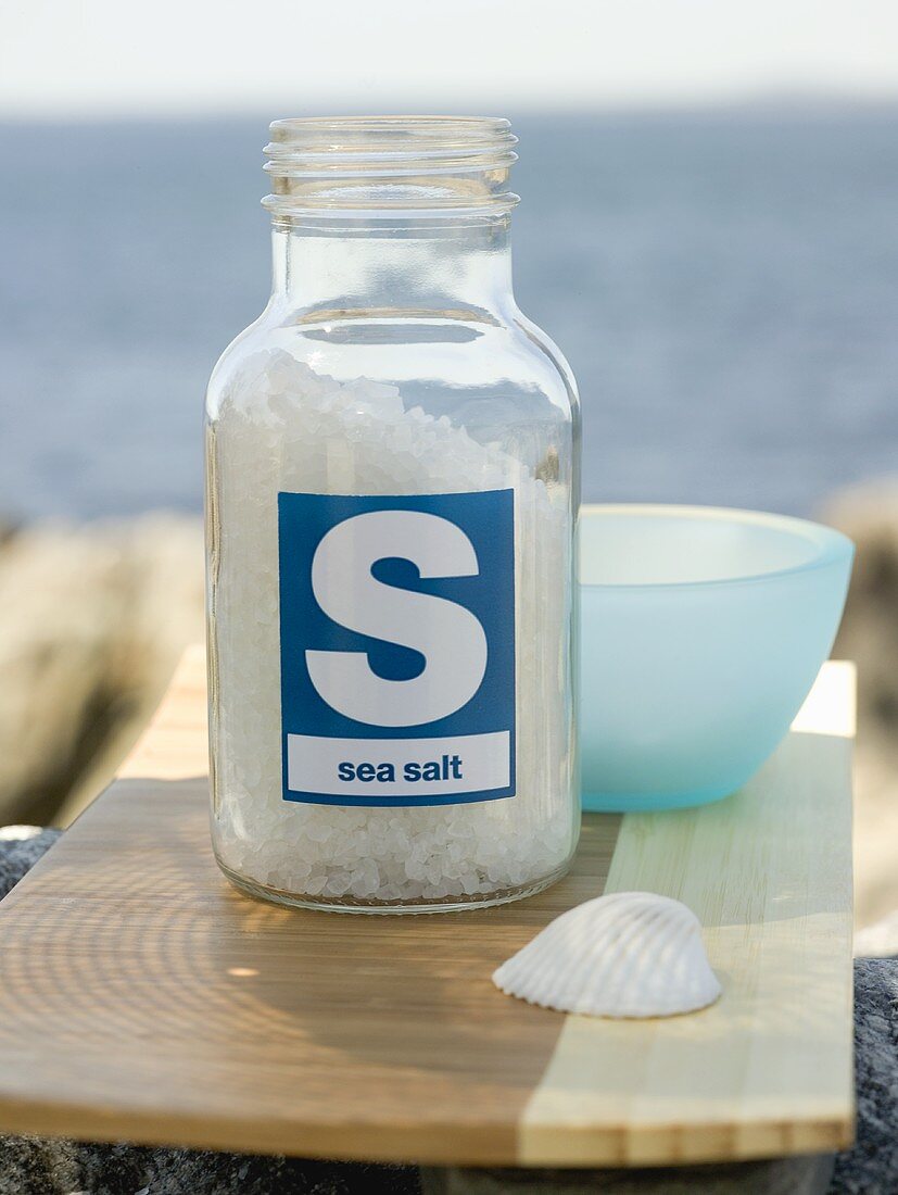 Sea salt in bottle on chopping board, sea in background
