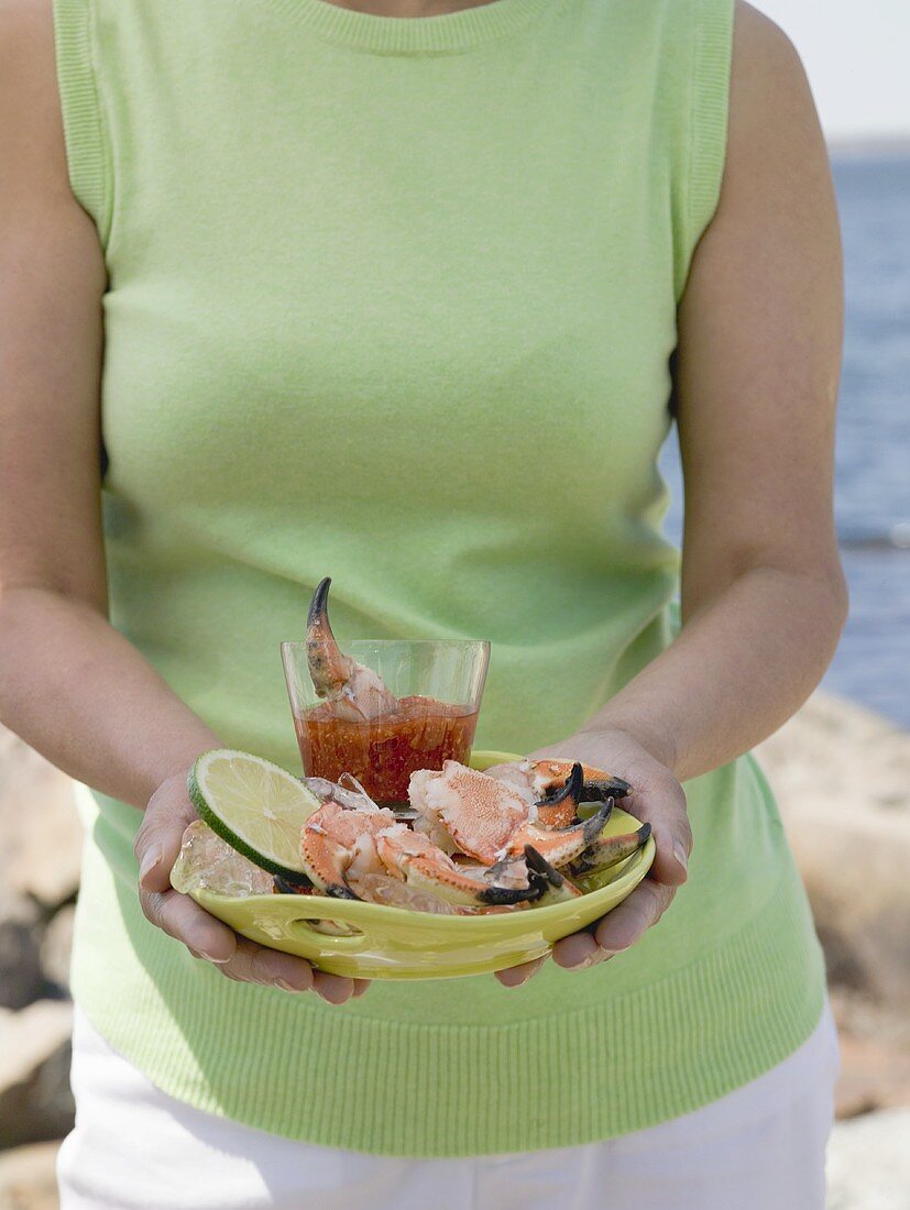 Frau hält Teller mit Krebsscheren und Dip am Strand