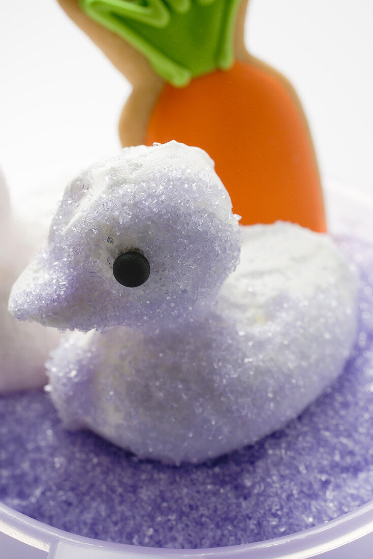 Meringue chick with purple sugar, carrot biscuit in background