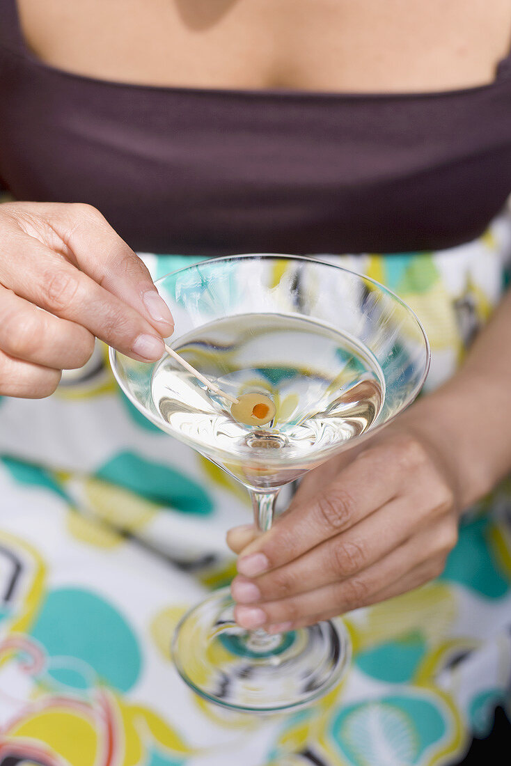 Frau hält Spiesschen mit grüner Olive im Martiniglas