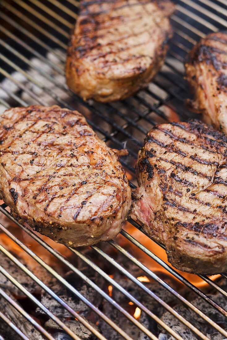 Several beef steaks on a barbecue grill rack