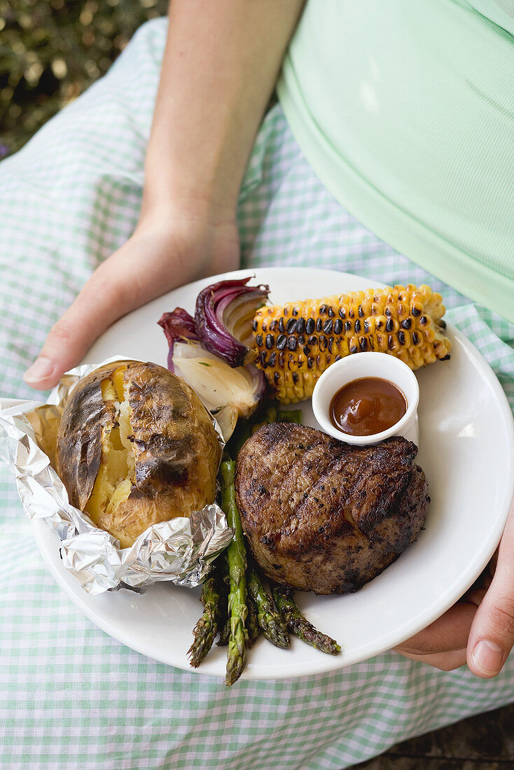 Woman holding a plate of grilled steak and accompaniments