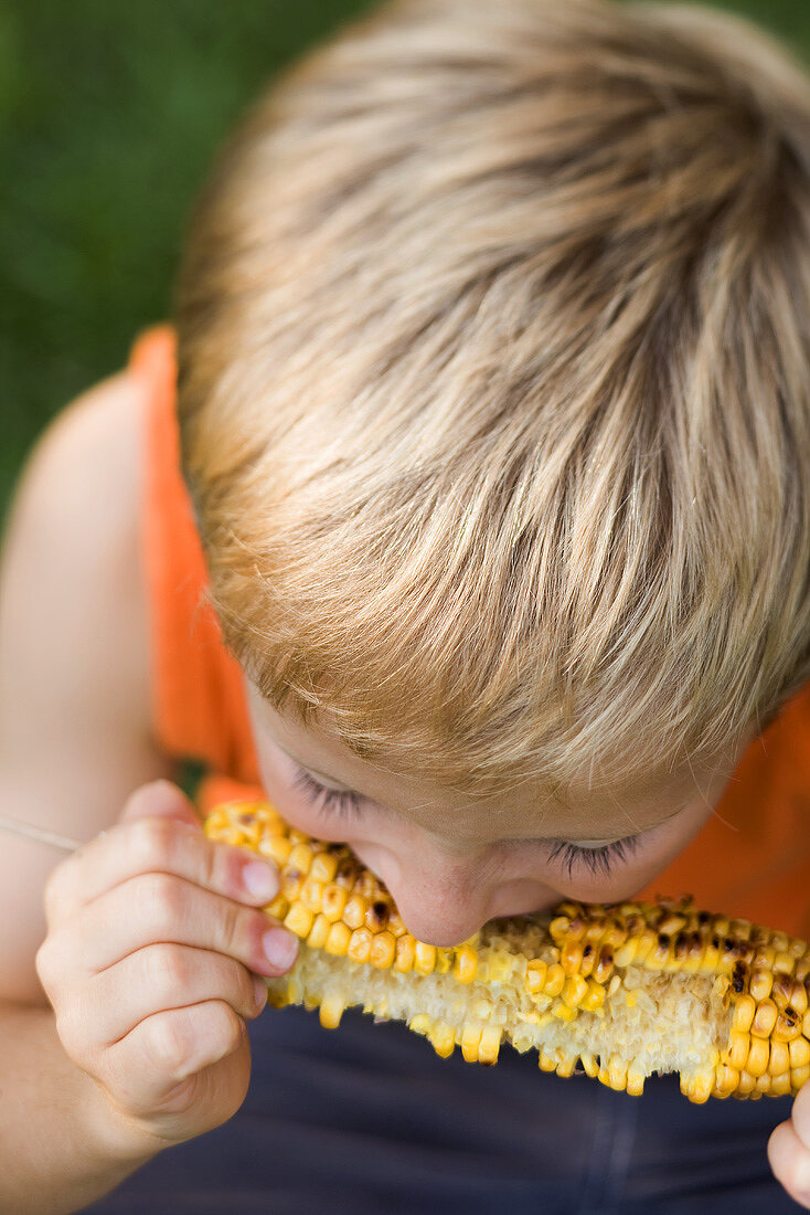 Kleiner Junge isst gegrillten Maiskolben