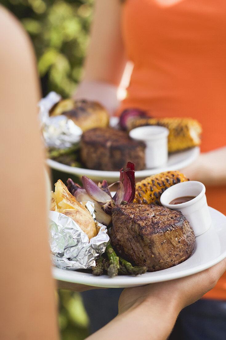 Two women holding plates of grilled steak & accompaniments