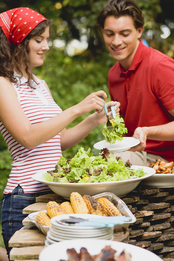 Young woman serving green salad at a barbecue