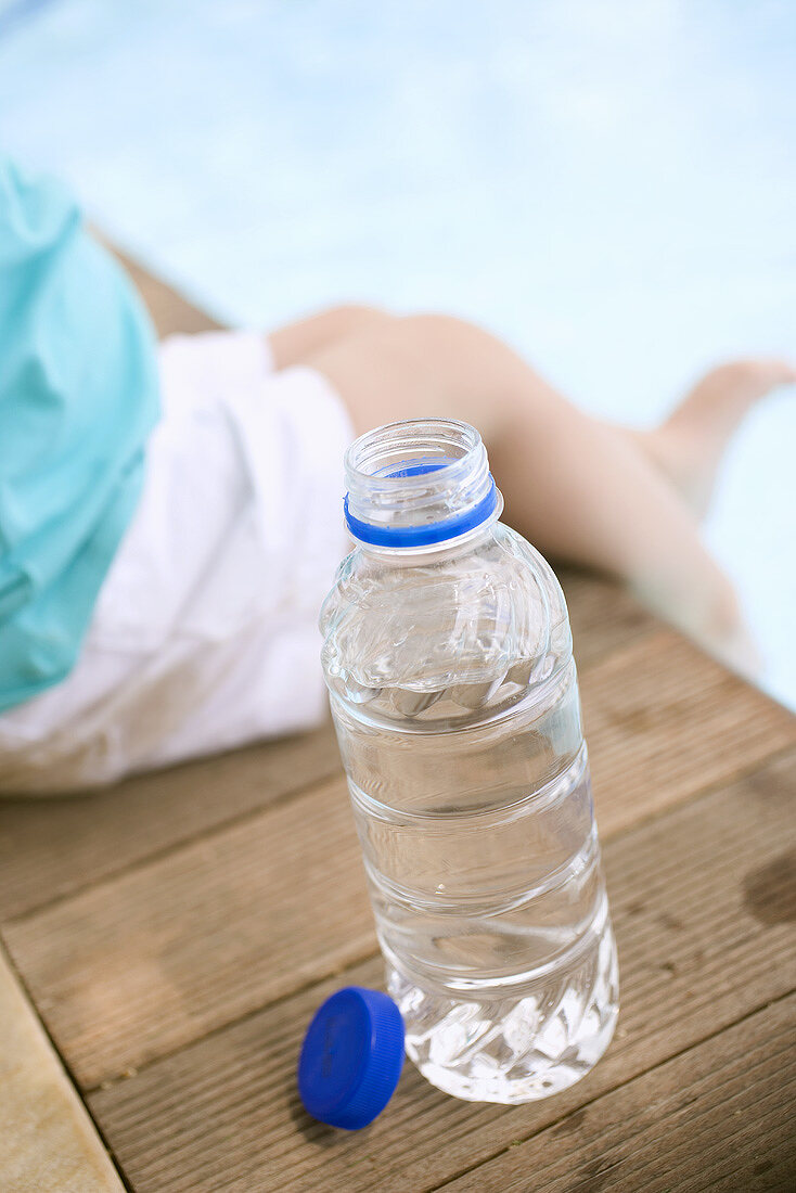Kind sitzt neben Wasserflasche am Schwimmbecken
