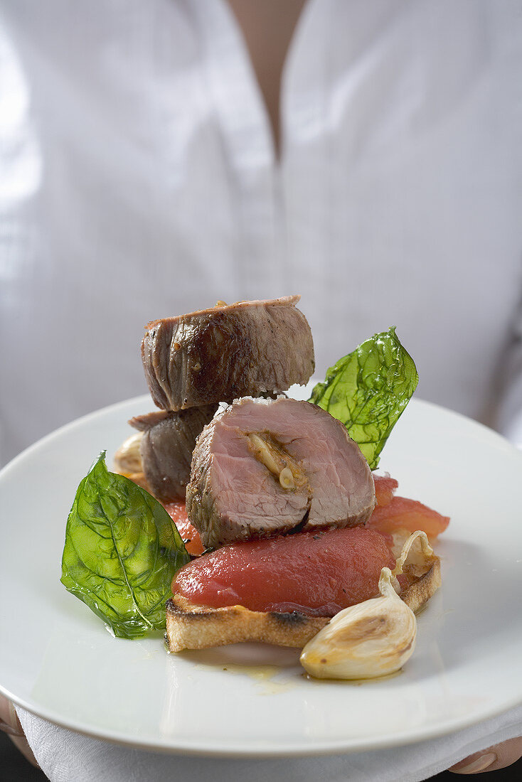 Woman serving pork fillet, tomatoes and basil on toast