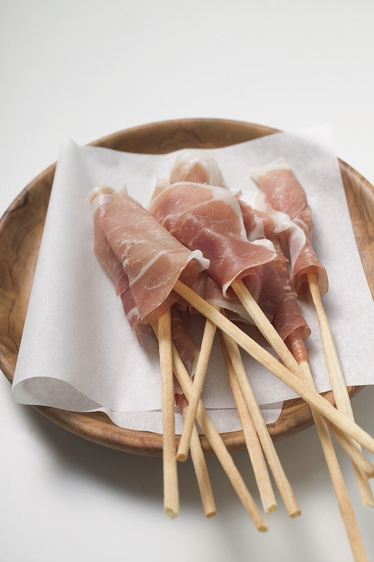 Grissini wrapped in raw ham on wooden plate