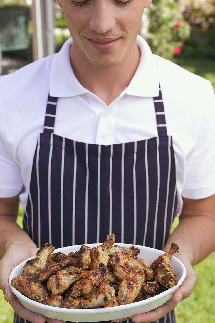 Man in apron holding grilled chicken wings