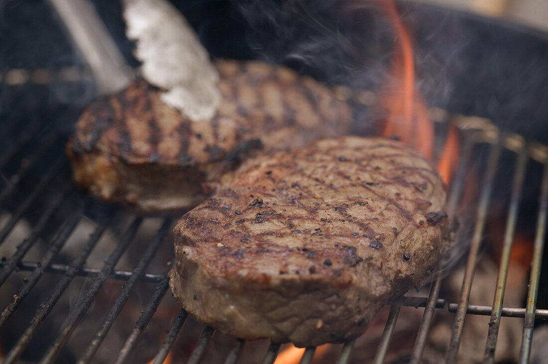 Beef steaks on a barbecue with barbecue tongs
