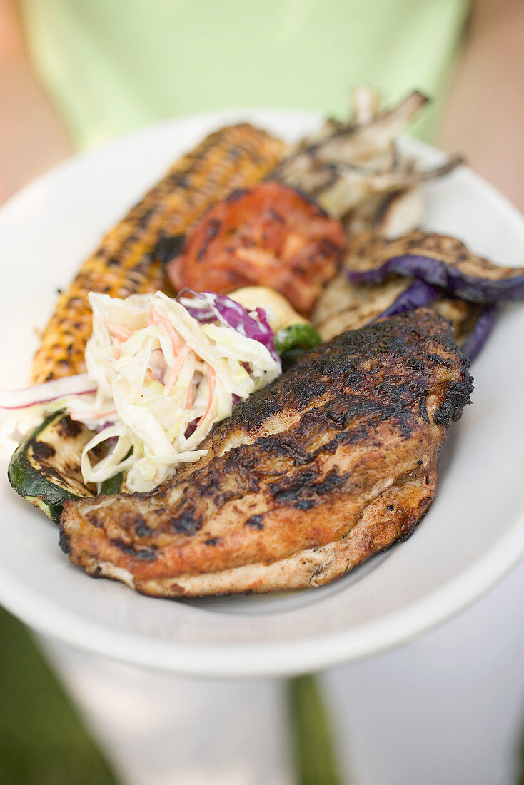 Woman holding plate of grilled chicken breast & accompaniments