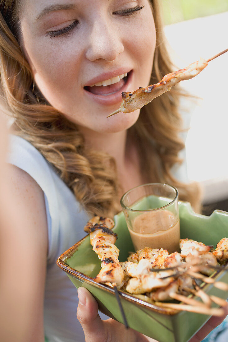 Woman eating grilled satay with peanut dip